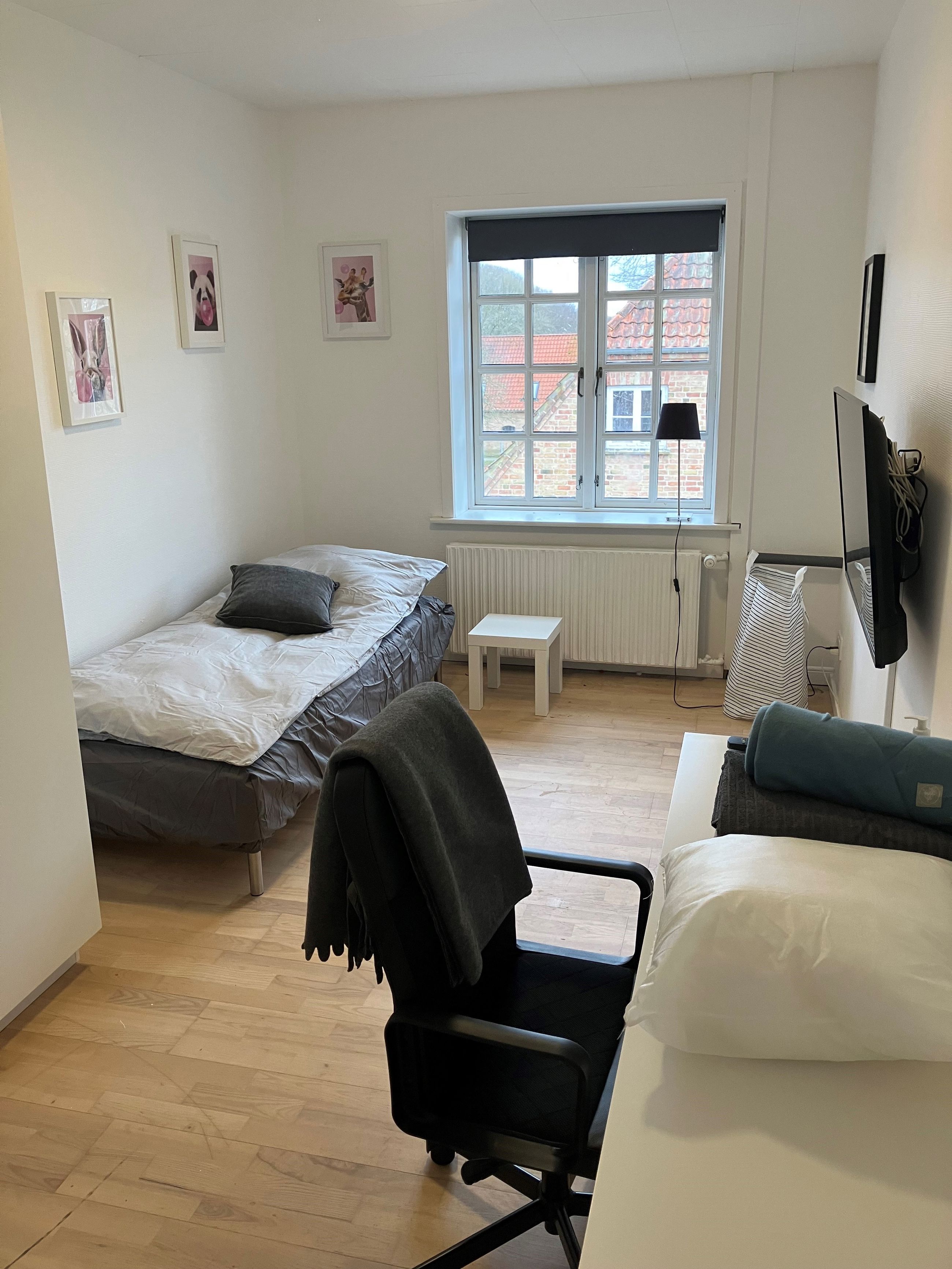 Et lyst værelse med seng, skrivebord, skrivebordsstol og tv