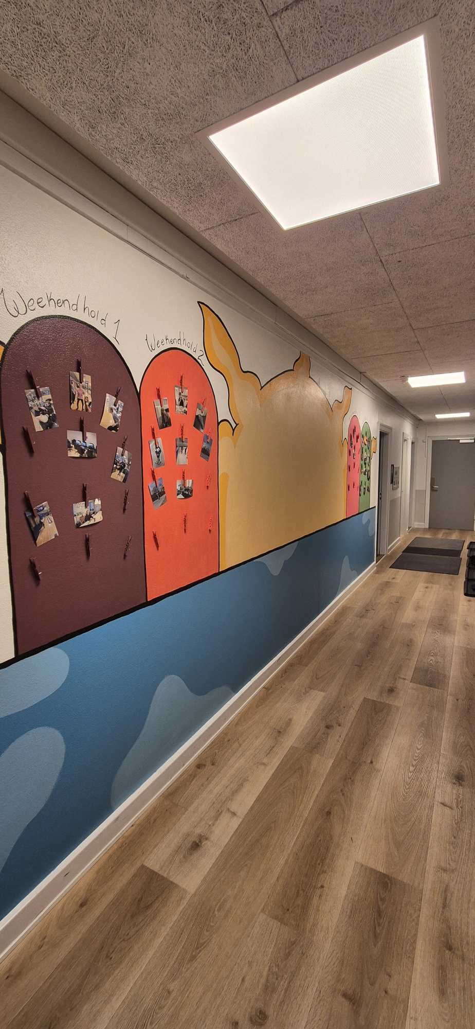 Lang gang med trægulv og farvestrålende vægge