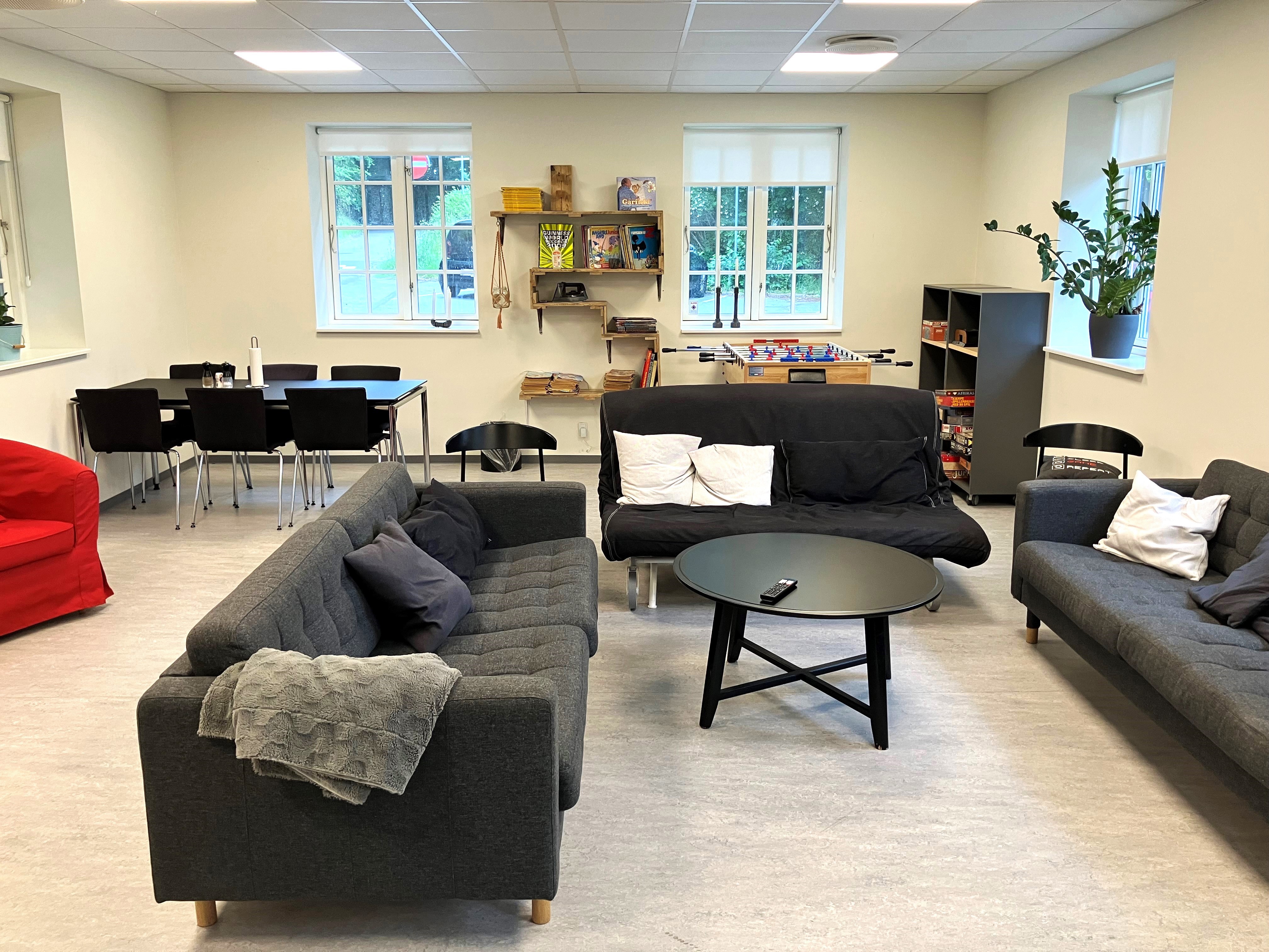 Opholdsstue med grå sofaer, bordfodboldbord og spisebord