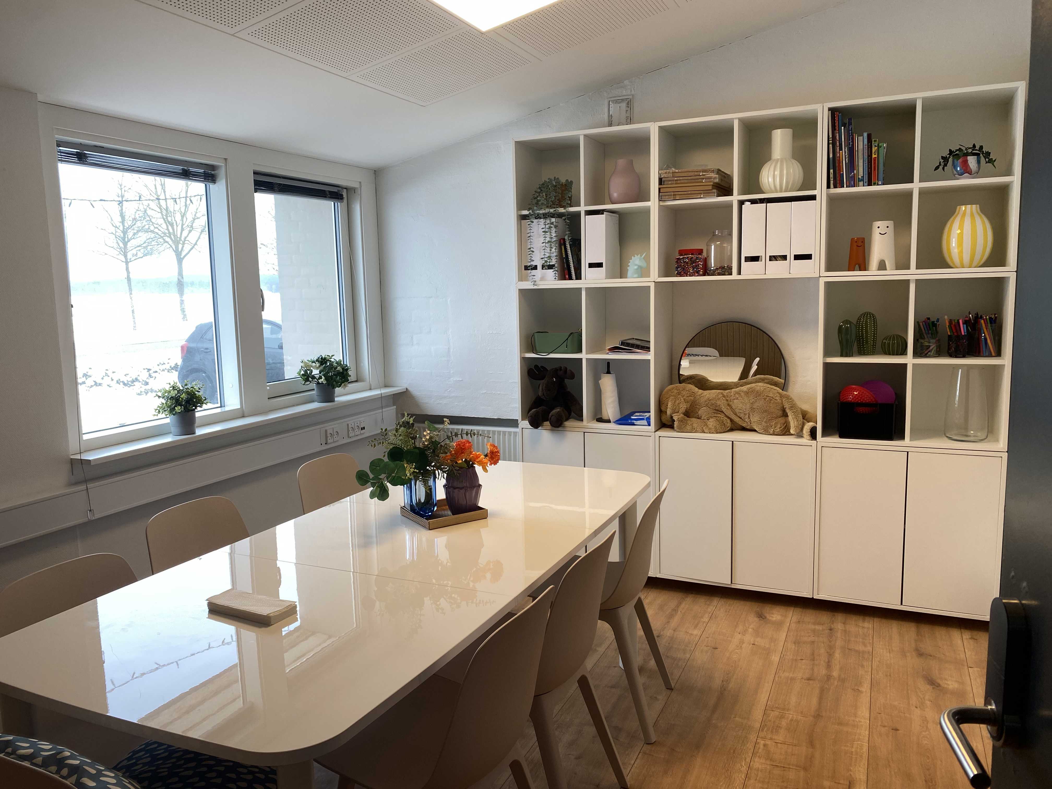 Mødelokale med mødebord og reol med pynteting